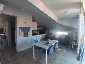 Eine moderne Küche mit Essbereich, einer Wanddekoration aus Makramee und einer Couch im Wohnbereich.