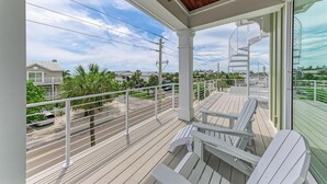 Uma varanda com cadeiras Adirondack brancas, teto de madeira e vista para uma área residencial com casas e palmeiras.