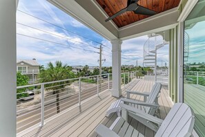 Ein Balkon mit weißen Adirondack-Stühlen, Holzboden und Blick auf eine Wohngegend mit Häusern und Palmen.