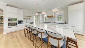 Uma cozinha moderna com armários brancos, uma ilha grande com banquetas e iluminação pendente.