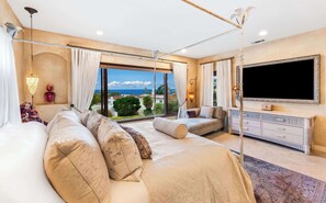 Ein Schlafzimmer mit einem großen Bett, einem Fernseher, einer Kommode und Meerblick.
