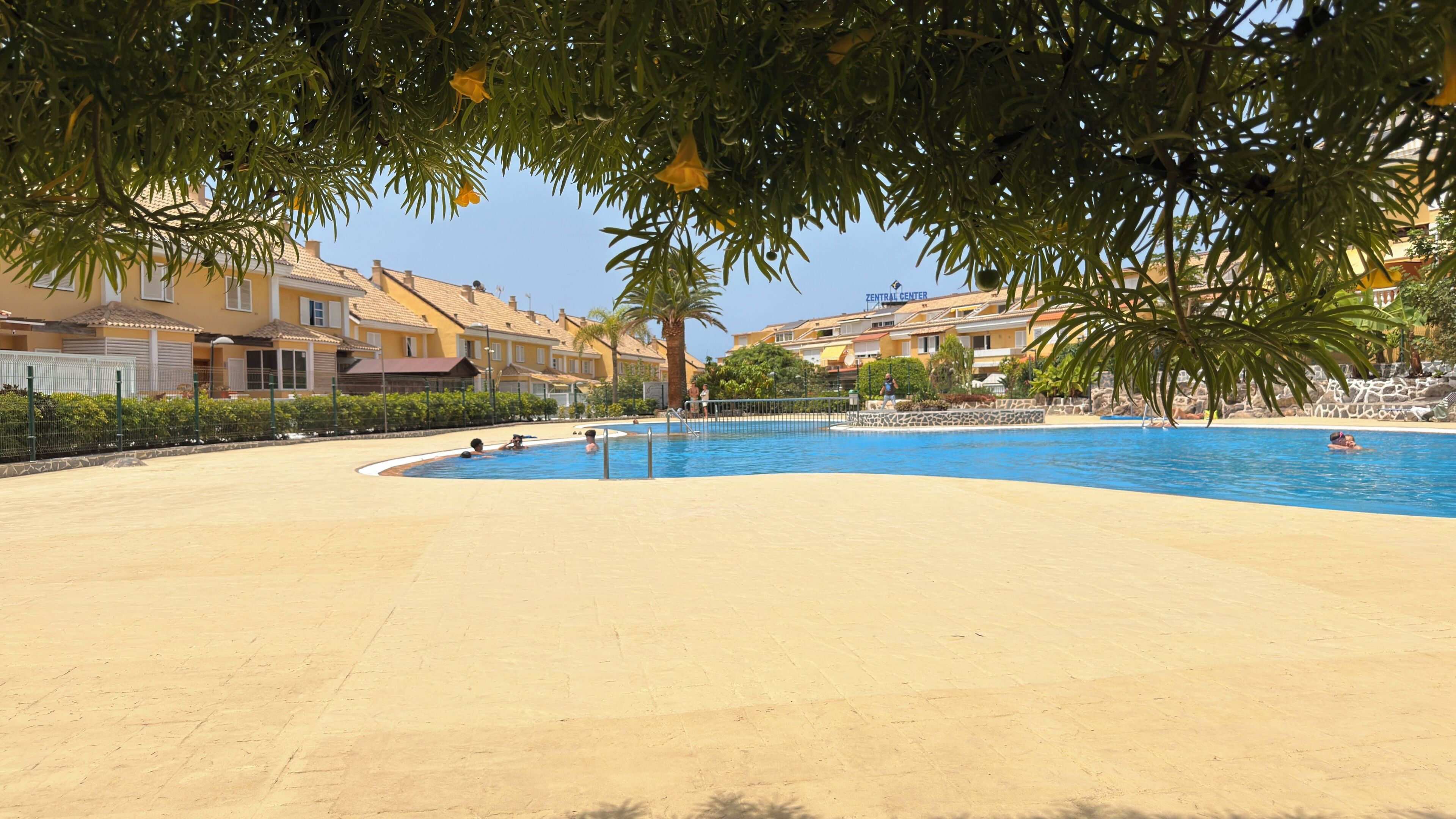 Una piscina con agua cristalina azul, rodeada de arena y una valla.