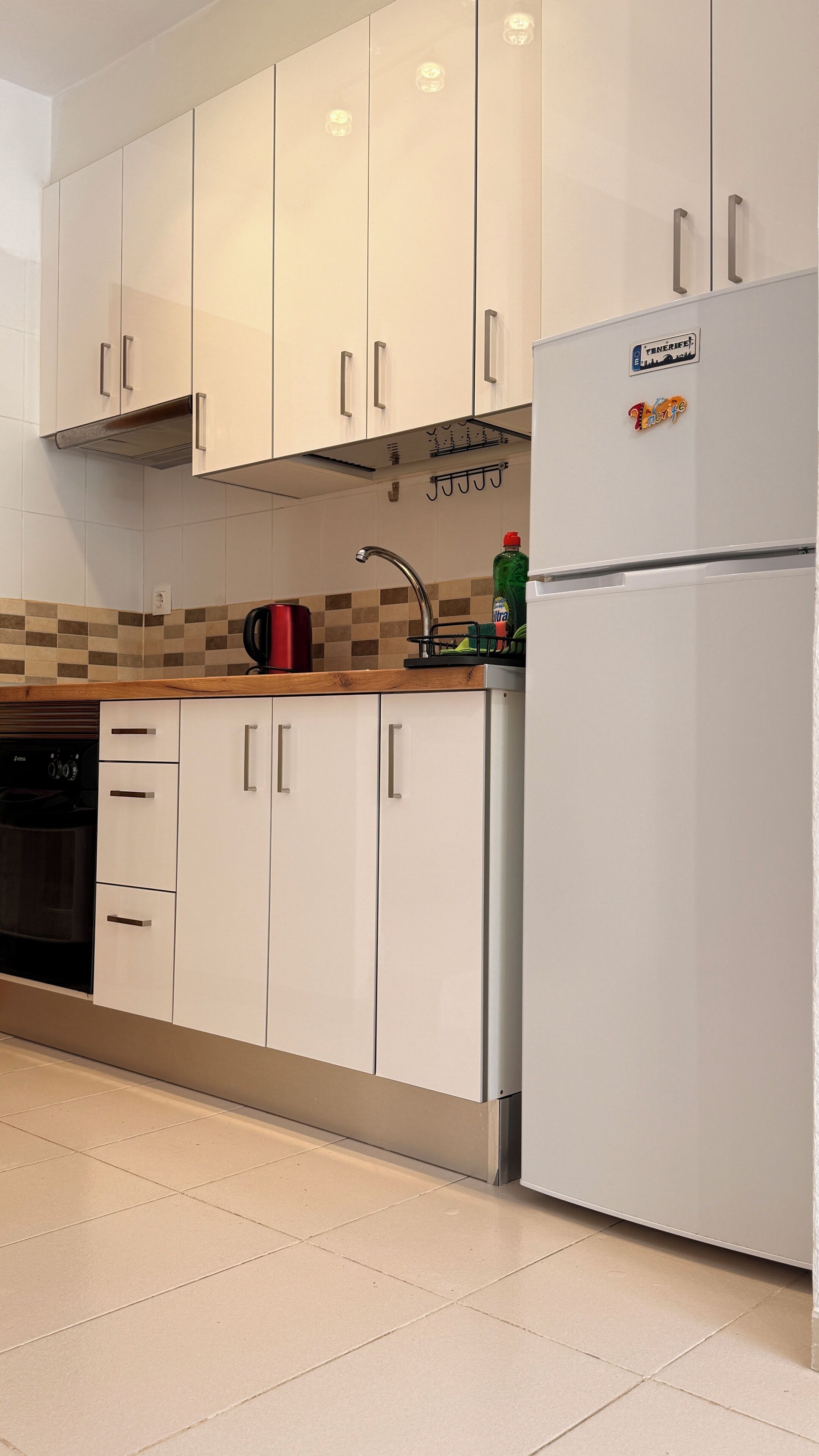 A kitchen with white cabinets, a stainless steel refrigerator, a dishwasher, and a tiled backsplash.
