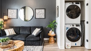 Una sala moderna con un sofá gris, un espejo redondo y una lavadora.