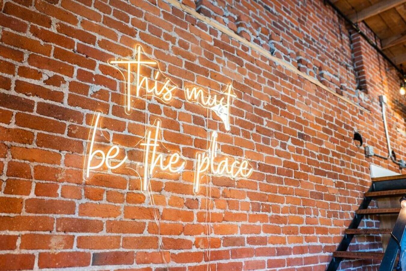 Een bakstenen muur met een neonbord waarop staat 'This must be the place'.