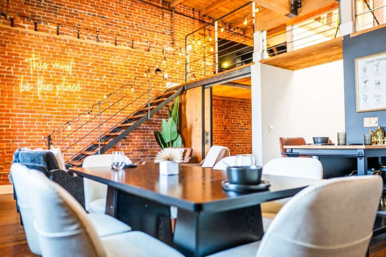 A modern interior with a brick wall, a staircase, and a dining area with chairs and a table.