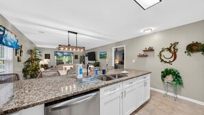 A modern kitchen with granite countertops, stainless steel appliances, and a dining area with wicker furniture. - First Floor condo on True Blue Golf course with Pool!!! (Pawleys Island)