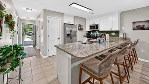 A modern kitchen with a granite island, bar stools, white cabinets, and a stainless steel refrigerator. - First Floor condo on True Blue Golf course with Pool!!! (Pawleys Island)