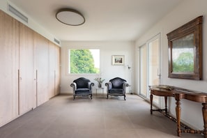 Ein geräumiges Zimmer mit hohen Decken, einem Holfischschrank, zwei Sesseln, einem kleinen Tisch und einem großen Spiegel.