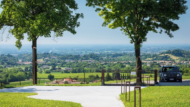 Ein gepflasterter Weg führt zu einem Tor mit Blick auf eine ländliche Landschaft und ein abgestelltes Fahrzeug.