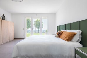 Ein modernes Schlafzimmer mit einem großen Bett, einem Holzschrank und Blick durch Glastüren.