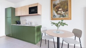 Una cucina moderna con mobili verdi, un forno a microonde e una macchina del caffè. C'è un tavolo da pranzo con sedie e un vaso con una pianta. Un quadro incorniciato è appeso al muro.