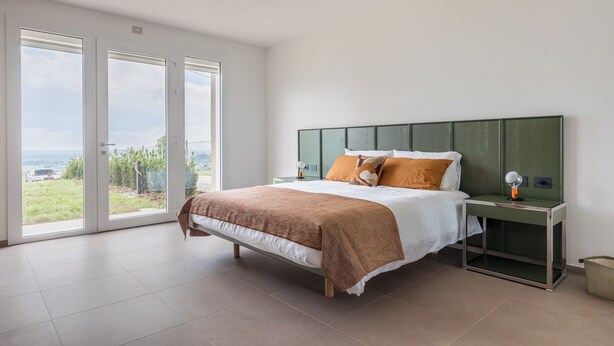 Una camera da letto con un letto, comodini e vista panoramica attraverso ampie porte scorrevoli in vetro.
