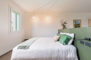 Ein Schlafzimmer mit Bett, Fenster, einem Bild und einer Wandsteckdose.