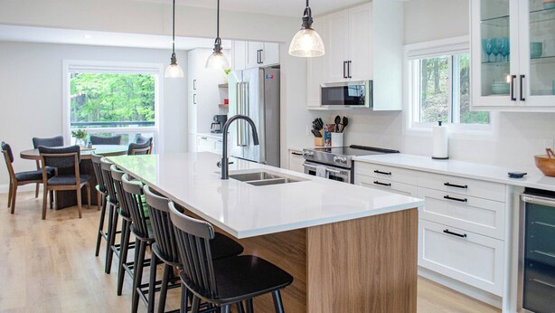 A modern kitchen with a central island, stainless steel appliances, and a dining area with bar stools. - Nature's Playground - Three Bedroom Cottage, Sleeps 6 (Gravenhurst)