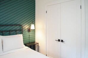 A bed with pillows, a bedside table, a lamp, and a white door.