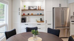 A modern kitchen with white cabinetry, a stainless steel refrigerator, and a dining table with chairs. - Nature's Playground - Three Bedroom Cottage, Sleeps 6 (Gravenhurst)