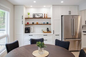 A modern kitchen with white cabinetry, a stainless steel refrigerator, and a dining table with chairs.