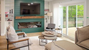 A modern living room with a fireplace, a flat-screen TV, and a view of the outdoors. - Nature's Playground - Three Bedroom Cottage, Sleeps 6 (Gravenhurst)