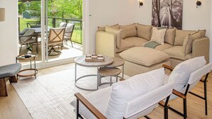 A living room with a sofa, armchairs, a coffee table, and a sliding glass door leading to an outdoor patio with chairs and a table. - Nature's Playground - Three Bedroom Cottage, Sleeps 6 (Gravenhurst)