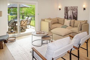 A living room with a sofa, armchairs, a coffee table, and a sliding glass door leading to an outdoor patio with chairs and a table.
