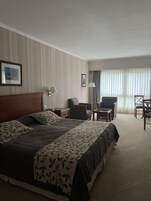 Habitación de hotel con una cama grande, un escritorio, una silla y un ventanal con cortinas.
