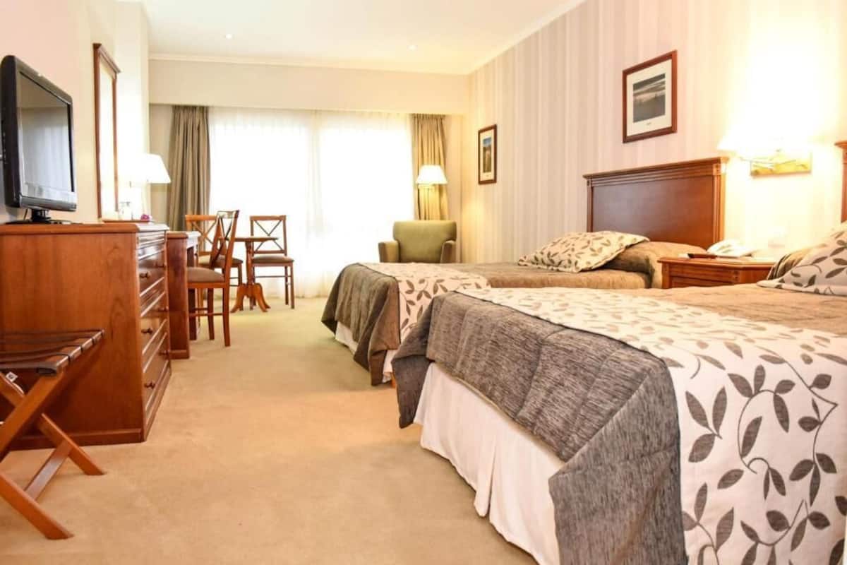 Una habitación de hotel con dos camas, un escritorio, una silla, un televisor y una lámpara.