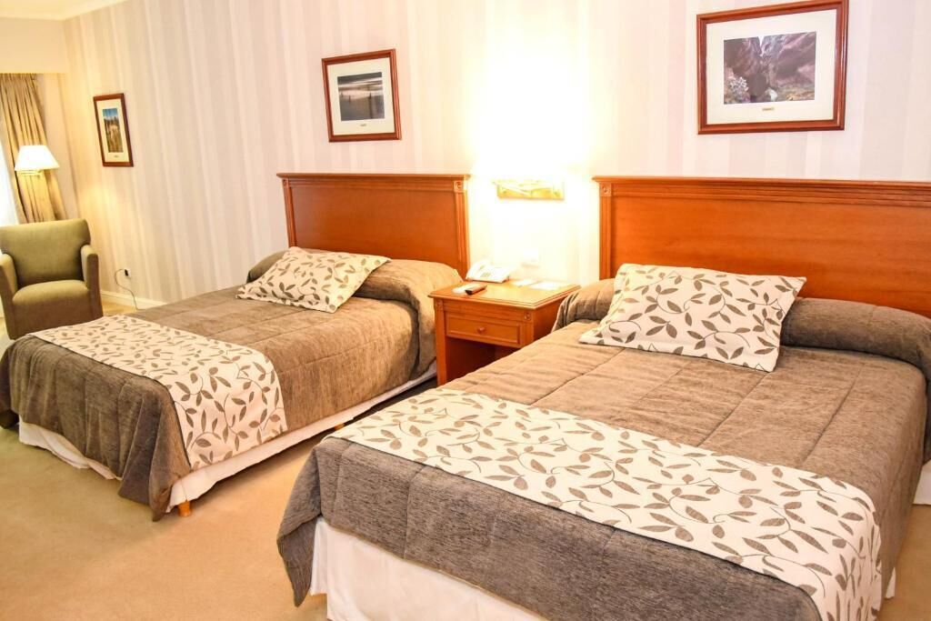 Una habitación de hotel con dos camas, una mesita de noche, una lámpara y cuadros en la pared.