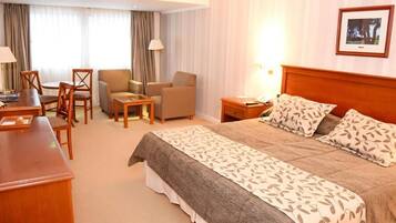 A hotel room with a bed, a desk, a chair, a small table, and a lamp.