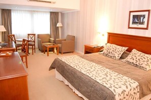 Una habitación de hotel con cama, escritorio, silla, una mesita y una lámpara.