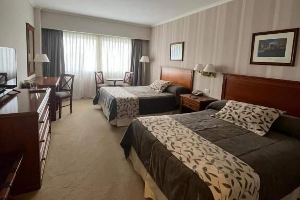 Habitación de hotel con dos camas, un escritorio, una silla y un televisor.