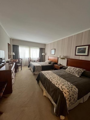 Habitación de hotel con dos camas, un escritorio, una silla y un televisor.