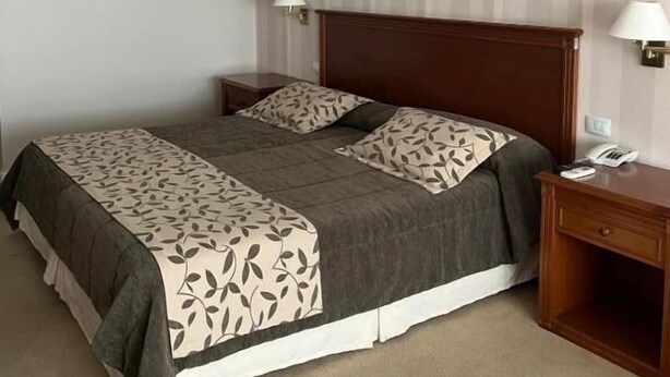 Une chambre d’hôtel comprenant un lit, des tables de chevet, une commode, une lampe, un tableau au mur et un appareil de climatisation.