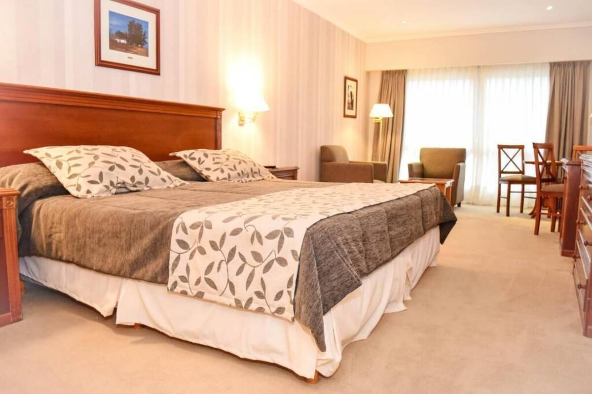 Habitación de hotel con una cama grande, dos sillas, un escritorio y una ventana con cortinas.