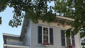 Une maison à deux étages avec un porche, une porte d’entrée ornée d’une guirlande et des jardinières aux fenêtres.