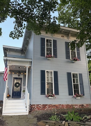 A two-story house with a porch, a front door with a wreath, and flower boxes on the windows.