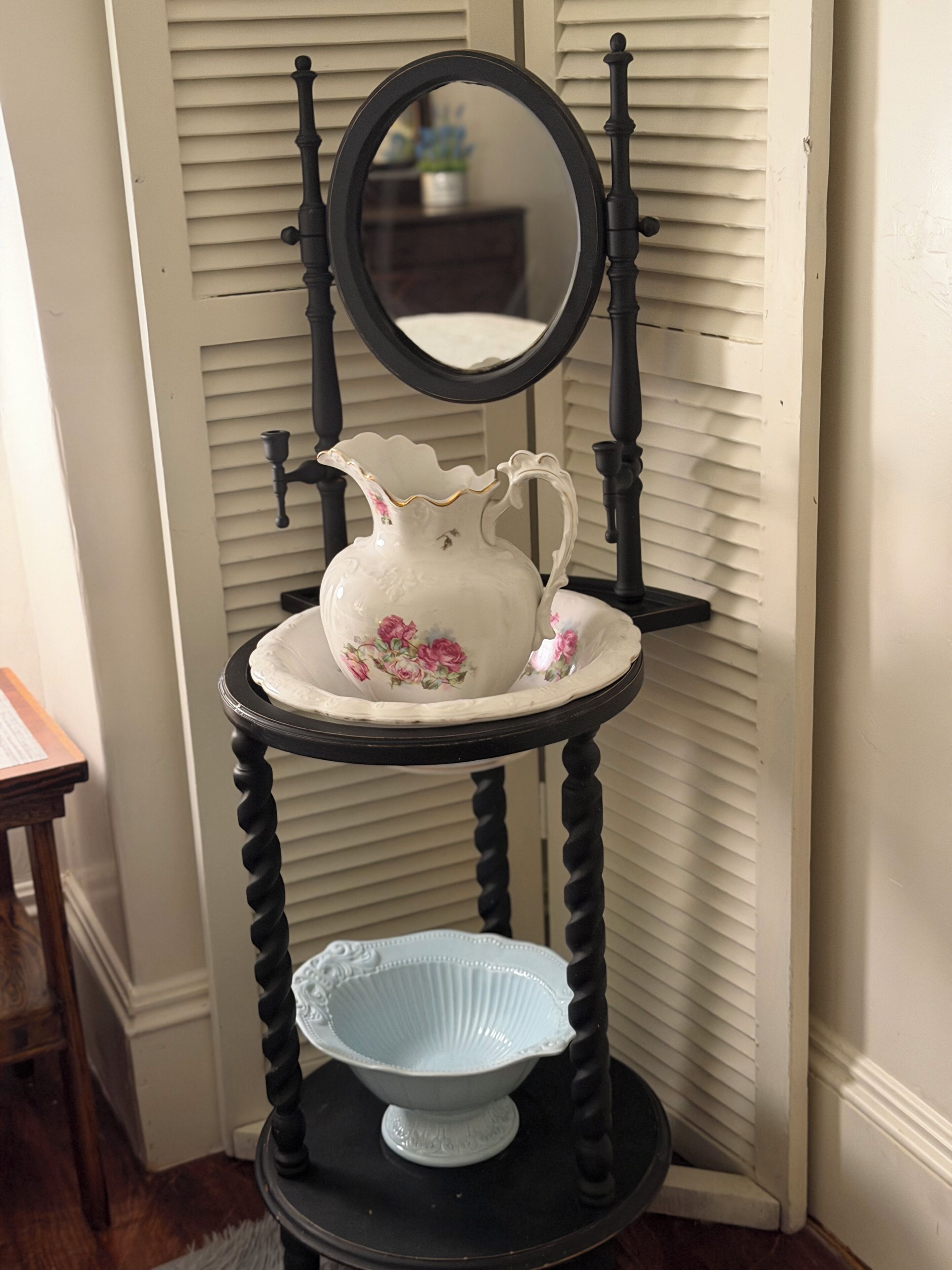 A black and white ceramic pitcher with floral designs on a black pedestal with a mirror above it.