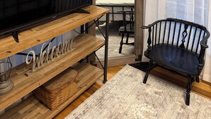 Une pièce avec un téléviseur posé sur un meuble en bois, une chaise, un lit et des rideaux.
