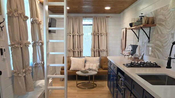 A loft-style bedroom with a bunk bed, a ladder, a sofa, and a small table. - Tiny Blanco Retreat Birdhouse (Wimberley)