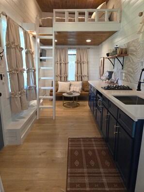 A loft-style bedroom with a bunk bed, a ladder, a sofa, and a small table.