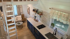 A loft-style bedroom with a bunk bed, a kitchenette with a stove and sink, and a dining area with a chair and table. - Tiny Blanco Retreat Birdhouse (Wimberley)