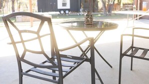 A round glass table with metal chairs, a lantern, and a building in the background. - Tiny Blanco Retreat Birdhouse (Wimberley)