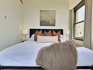 A hotel room with a large bed, a headboard with decorative pillows, a wall-mounted artwork, and a window with curtains. - Sunlit downtown loft, walk to theatres (Birmingham)