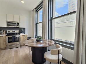 Une cuisine moderne équipée d’appareils électroménagers en acier inoxydable, une table à manger ronde et une vue sur la ville grâce à de grandes fenêtres.