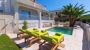 Zona de piscina amb gandules, una palmera i un edifici amb balcons.