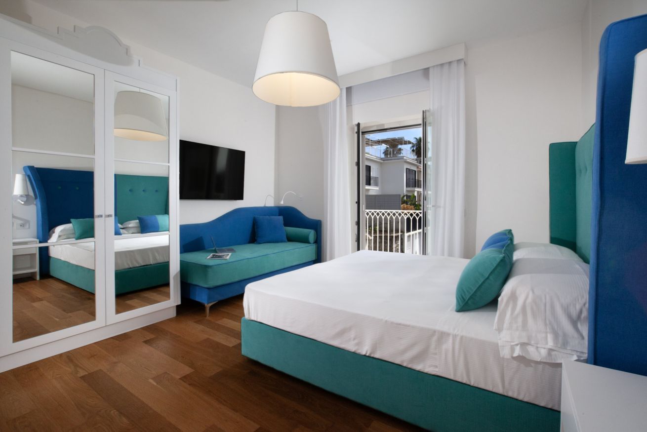 A hotel room with a bed, a sofa, a TV, and a balcony view.