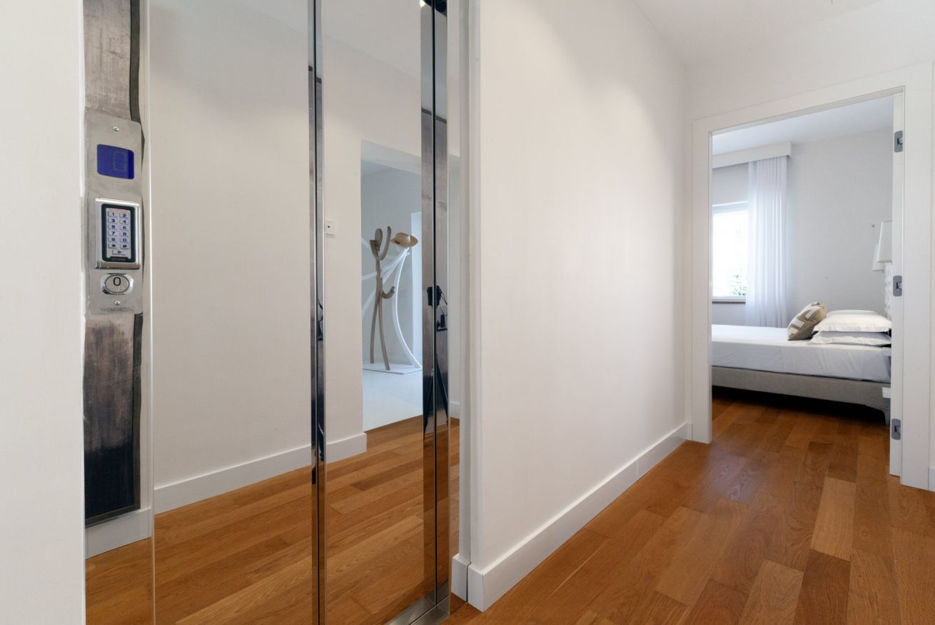 Une chambre d’hôtel moderne avec un plancher en bois, un lit avec une literie blanche et une porte de séparation en verre.