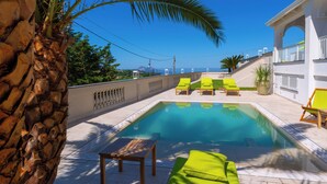 Zona de piscina amb vista despejada al cel, una palmera i un edifici amb balcó.