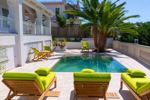 A pool area with lounge chairs and a palm tree. - Nevada Infinity Villa | Pool, Terrace, View of Capri (Massa Lubrense)