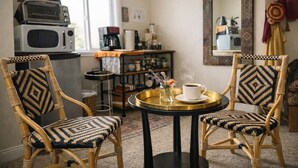 Ein gemütliches Zimmer mit Korbmöbeln, einem kleinen runden Tisch mit Tasse und Blumen, einer Mikrowelle und einer Kaffeemaschine.